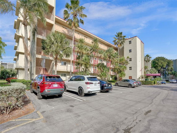Outdoor parking area in front of a multi-story building with palm trees.