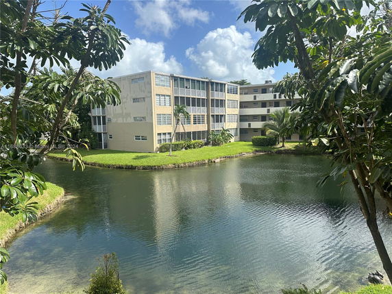 View of a multi-story building with a pond and trees in the foreground.