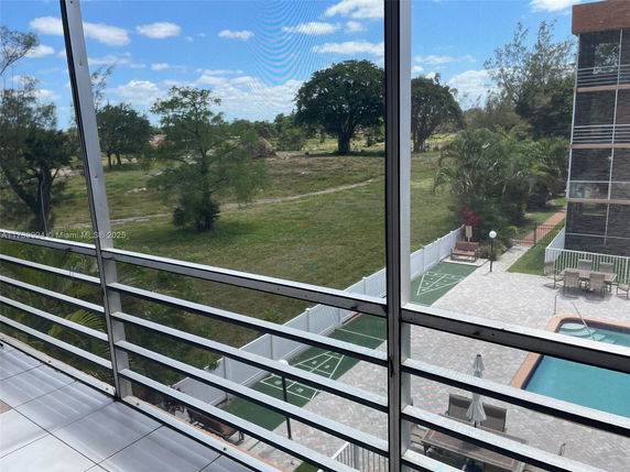 View of surrounding area from building balcony with pool and greenery.