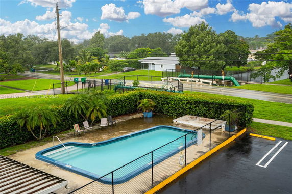 Outdoor swimming pool with a surrounding fence and few chairs.