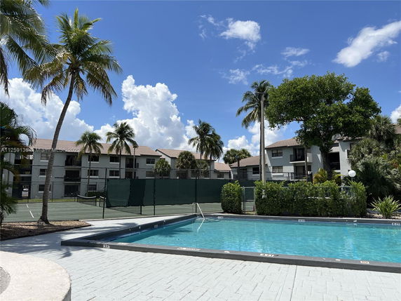 Outdoor swimming pool with adjacent buildings and palm trees.