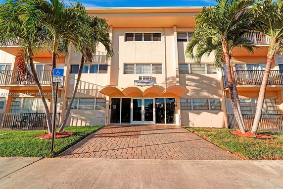 Front view of a multi-story building with a paved entrance and palm trees.