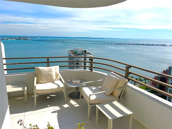 Outdoor balcony with chairs overlooking a large body of water and a distant bridge.