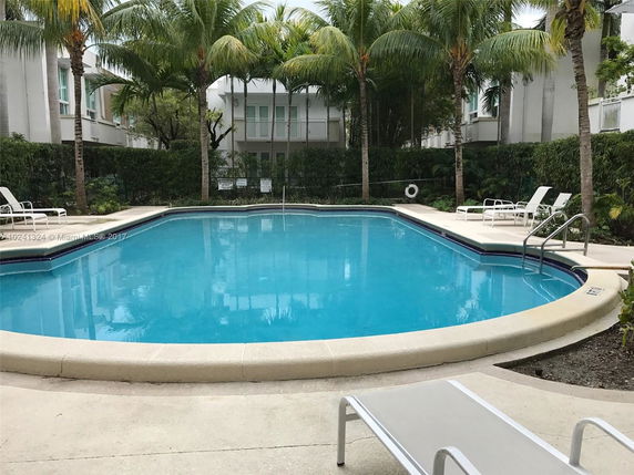 Outdoor swimming pool with surrounding palm trees and poolside chairs.