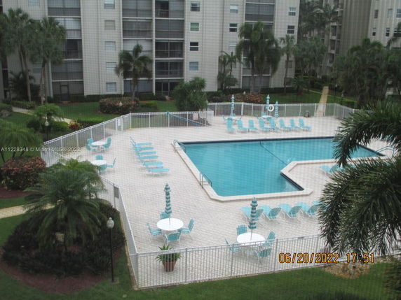View of a multi-story residential building with a swimming pool area surrounded by lounge chairs and umbrellas.