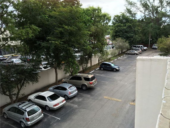 View of a parking lot with several parked cars and surrounding trees.