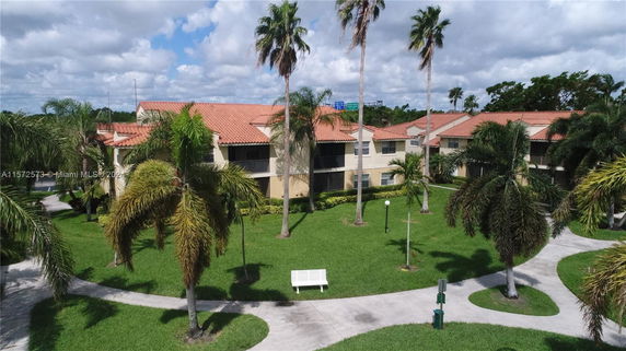 Front view of a residential building with red-tiled roofs, surrounded by palm trees and landscaped pathways.