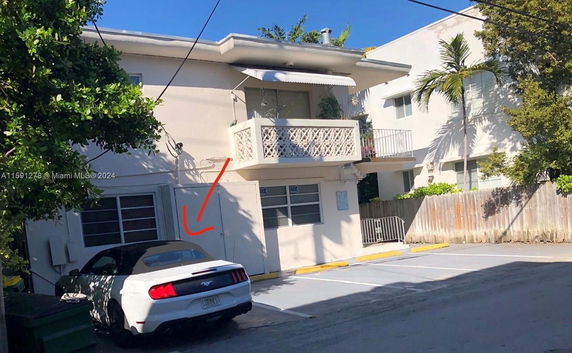 Outdoor parking area with a car parked beside a two-story building.