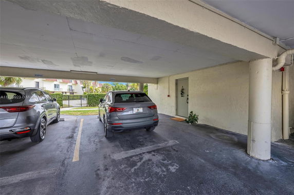 Covered parking area with two parked cars and a door leading to the building.