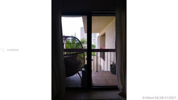 View from a balcony with an outdoor chair and railing, showing surrounding buildings and vegetation.