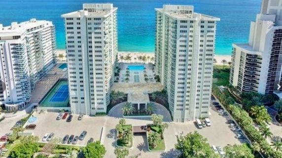 Aerial view of high-rise buildings near the ocean with a visible swimming pool and tennis court.