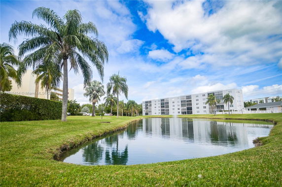 View of a multi-story residential building with a pond and palm trees in the foreground.