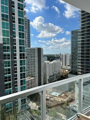 View of cityscape with multiple tall buildings and a blue sky seen from a balcony.