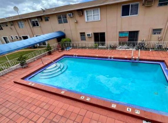Outdoor swimming pool with surrounding patio and residential building in the background.