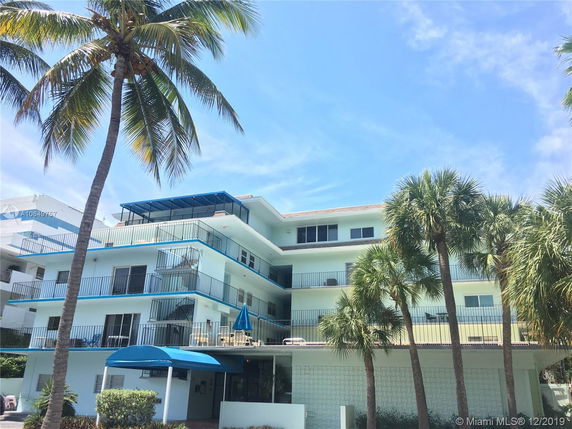 Front view of a multi-story building with balconies and a blue awning.