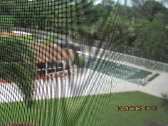 View of a swimming pool and a patio area with trees in the background, as seen through a mesh screen.