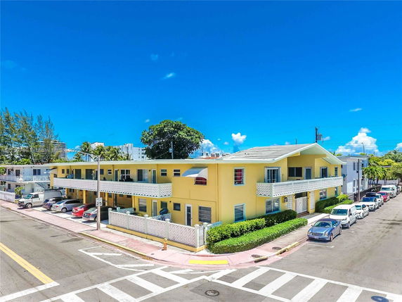 Front view of a two-story yellow building at a street corner, with parking space and a tiled roof.