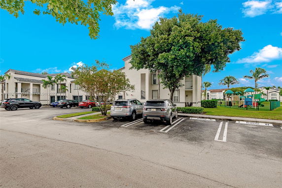 Parking area in front of a residential building with multiple cars and trees.