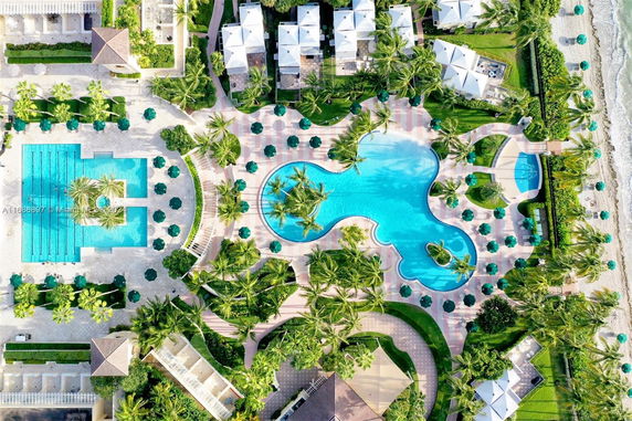 Aerial view of an outdoor swimming pool area surrounded by greenery and structures.