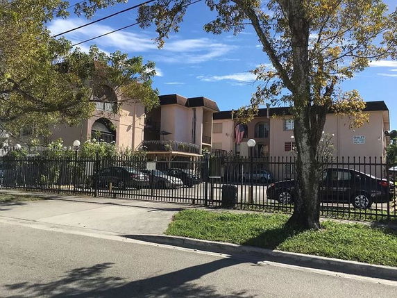 Front view of a multi-story residential building with parking area and fence.