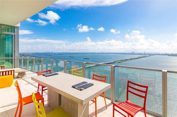 Panoramic view from a balcony with colorful chairs and a table overlooking a city skyline and a body of water.