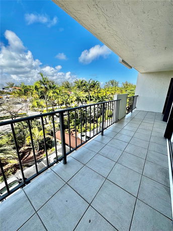 View from a balcony with metal railings overlooking trees and a parking area.