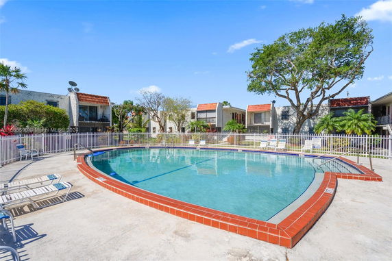Outdoor swimming pool surrounded by a fence with nearby residential buildings.