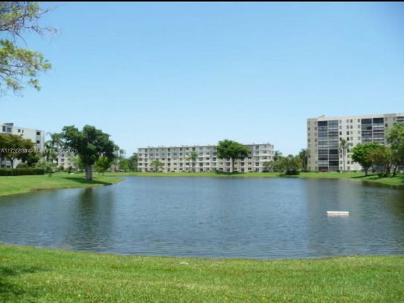 View of residential buildings across a lake with trees and grass.
