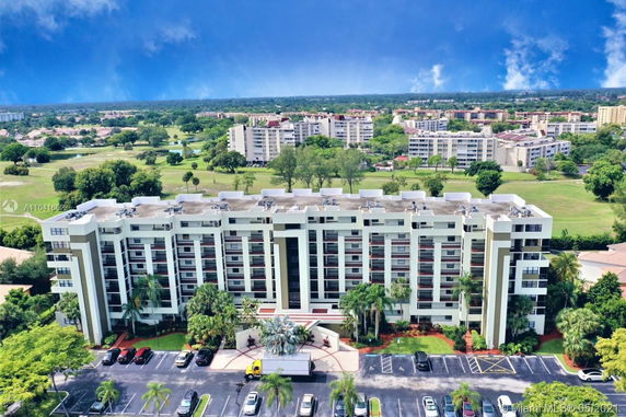 Aerial view of a multi-story residential building with surrounding greenery and other buildings in the distance.