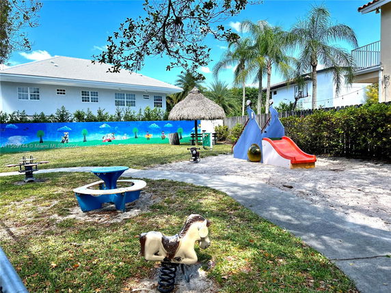 Playground with slides, spring riders, and a thatched hut, surrounded by trees.
