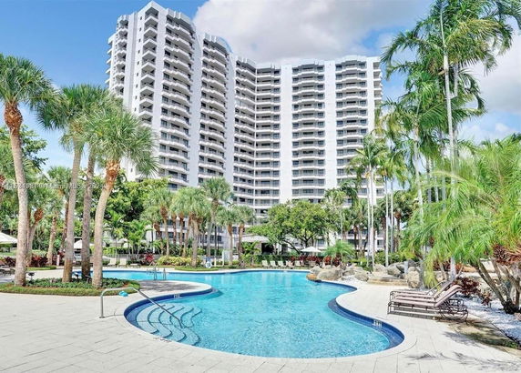 Tall residential building with an outdoor swimming pool surrounded by palm trees.