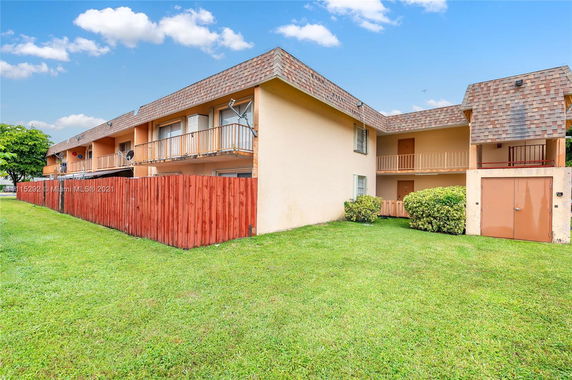 Front view of a two-story residential building with balconies and a wooden fence.