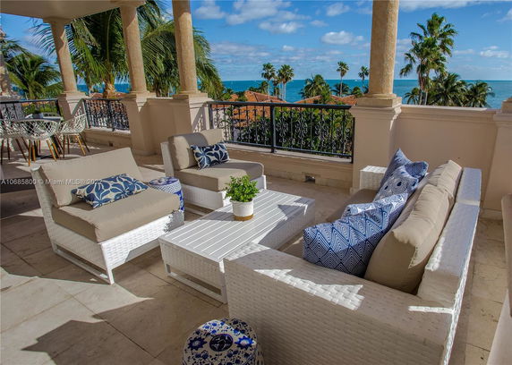 Outdoor patio with wicker furniture and ocean view from a balcony.