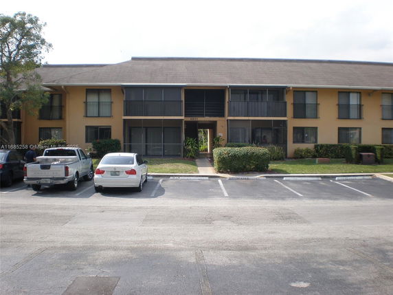 Front view of a two-story apartment building with multiple balconies and parking area in front.