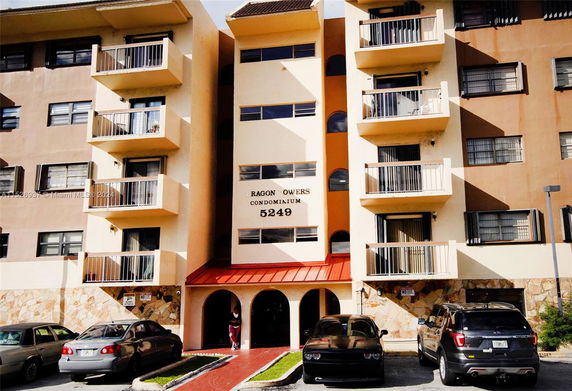 Front view of a multi-story condominium building with balconies and a red-roofed entrance.