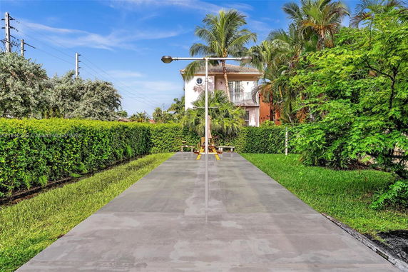 Outdoor view of a pathway leading to a house surrounded by lush greenery and palm trees.