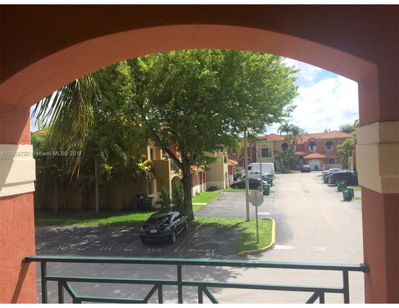 View from a building showing a residential street with parked cars and trees.