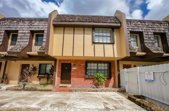 Front view of a two-story townhouse with a brick and wood facade, featuring a shake-style roof.