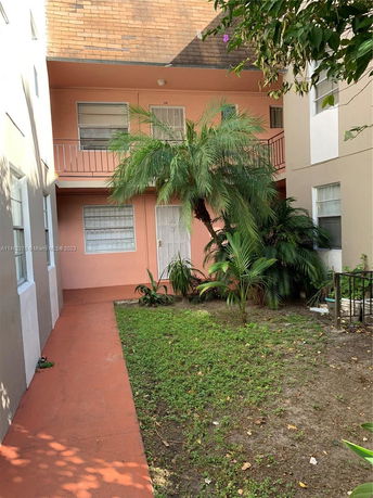 Front view of a two-story building with a pink facade and a garden area with palm plants.