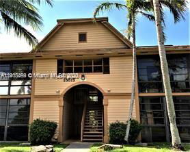 Front view of a two-story wooden building with an arched entrance and surrounding palm trees.