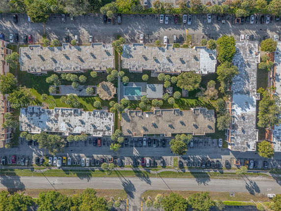 Aerial view of multiple buildings with flat rooftops, parking areas, and surrounding greenery.