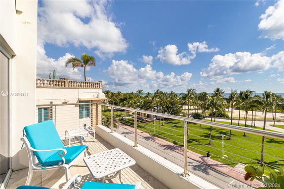 View from a balcony overlooking greenery and a beach in the distance.