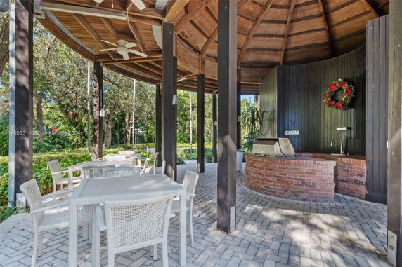 Outdoor patio area with tables, chairs, and a brick barbecue setup under a wooden roofed structure.