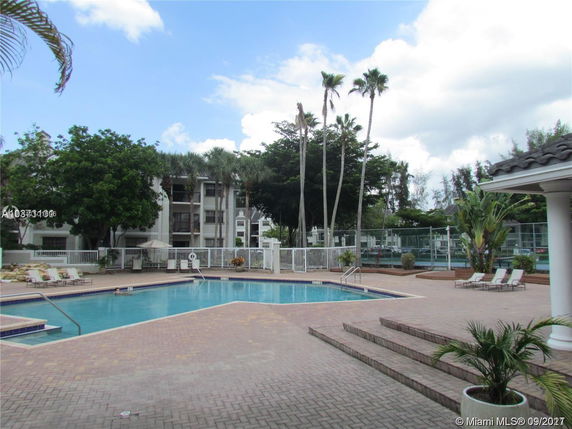 Outdoor swimming pool area with surrounding buildings and palm trees.
