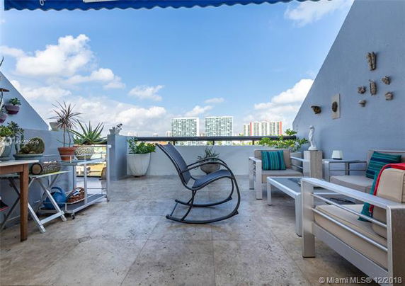 Rooftop terrace with seating and potted plants, featuring a view of distant buildings.