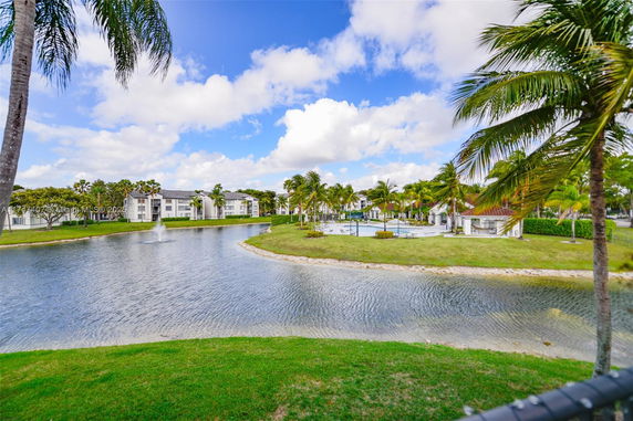 View of residential buildings beside a pond with palm trees and a water fountain.