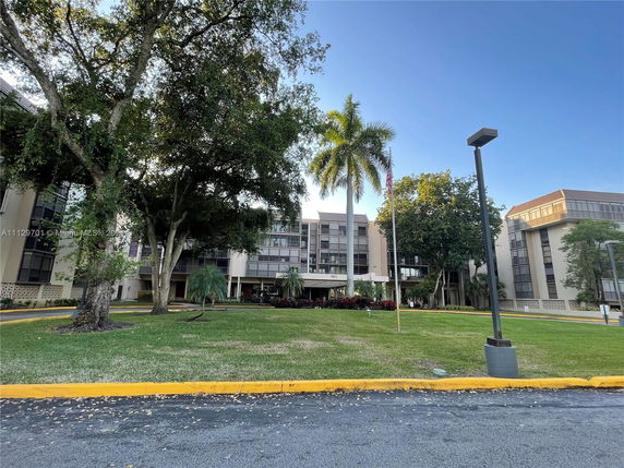 Front view of a multi-story residential building with large windows and surrounding greenery.
