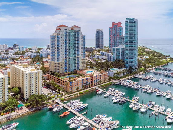 Aerial view of high-rise buildings near a marina with multiple boats docked, overlooking the ocean.