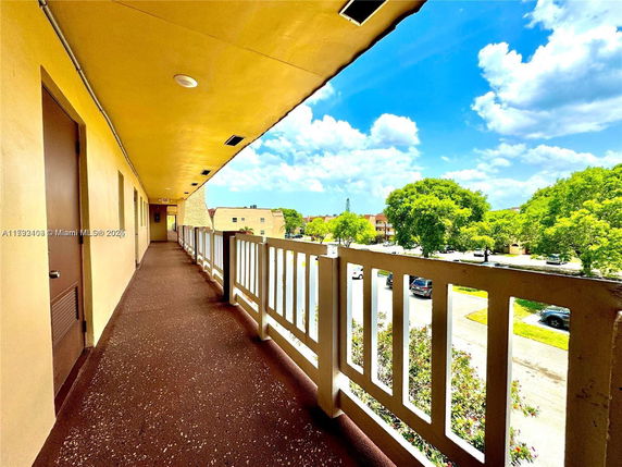 Exterior walkway view from a building with railings overlooking trees and nearby structures.