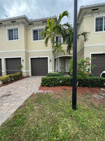 Front view of a two-story house with a garage and palm trees.